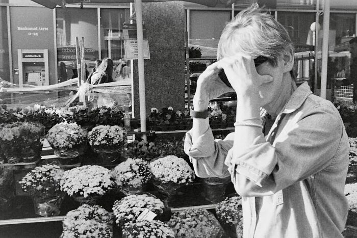 Person shielding eyes from sunlight near outdoor flower stand, capturing street moments that feel like magic in daily life.