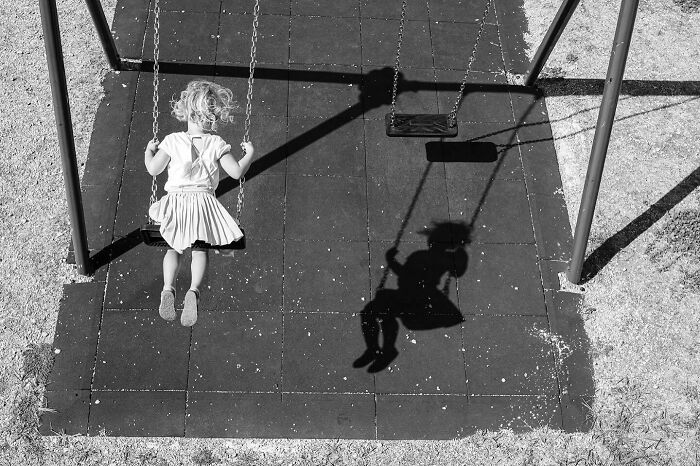 A child swinging in a playground captures the marvels of daily life and magical street moments in black and white.