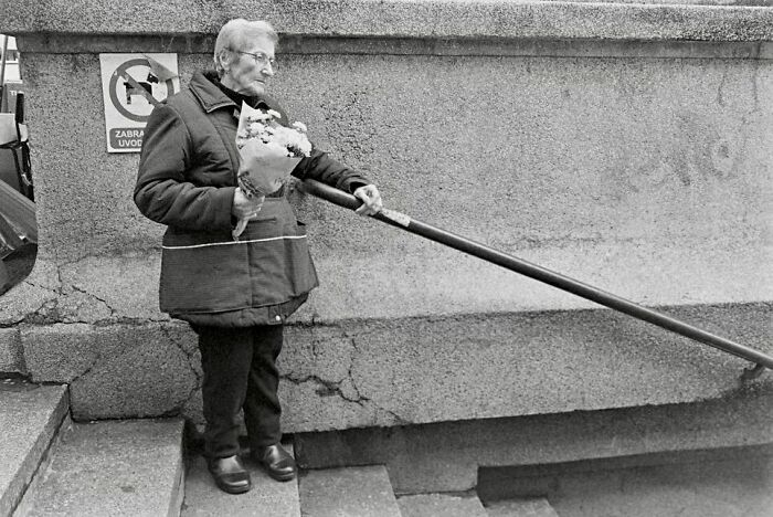 Elderly woman holding flowers pauses on urban stairs, capturing street moments that feel like magic in daily life.