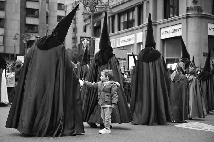 Child reaching out to figures in tall cloaks during a magical street moment capturing the marvels of daily life.