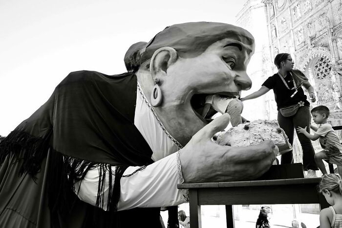 Giant puppet eating bread during a street moment that captures the marvels of daily life and magic.