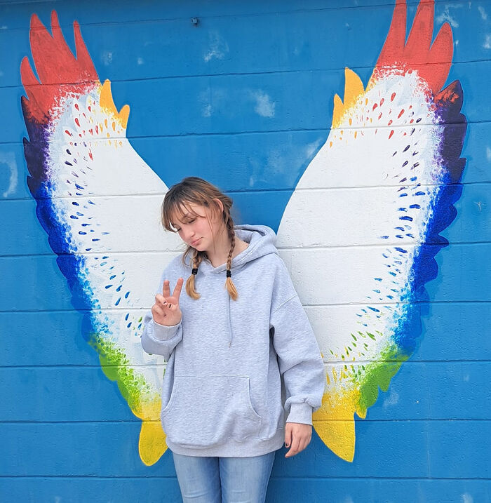 Teen girl posing in front of colorful painted wings on a blue wall symbolizing innocence before disturbing tactic incident. Teen girl posing in front of colorful painted wings on a blue wall symbolizing innocence before disturbing tactic incident.