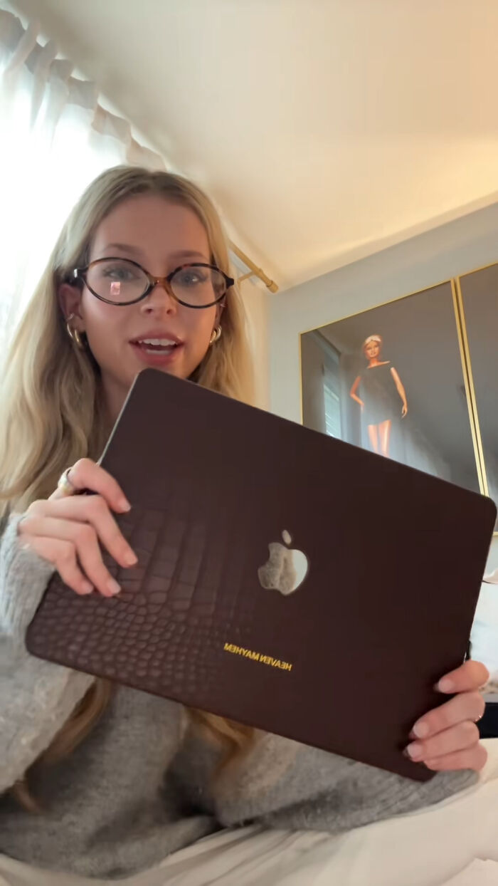 Young woman holding laptop with leather case, sharing highly recommended Christmas gifts in a cozy room setting.