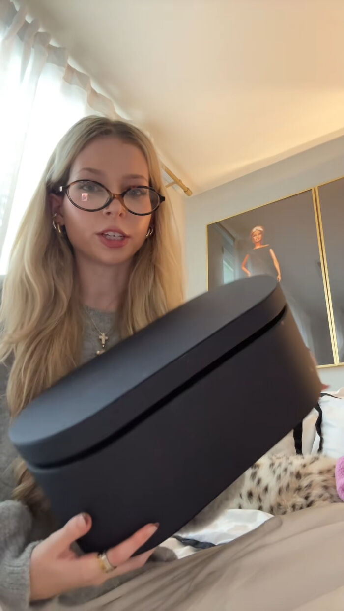 Young woman with glasses holding a black box, sharing Christmas gifts people can't recommend more in a cozy room setting.