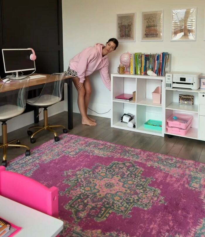 Woman in a pink hoodie in a colorful homeschool room with shelves and a computer, illustrating viral homeschool clip topic.
