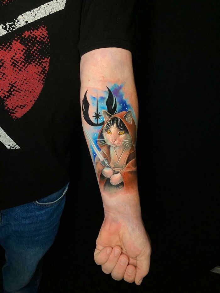 Colorful pet tribute tattoo of a cat dressed as a Jedi, blending vibrant details and starry background on forearm.