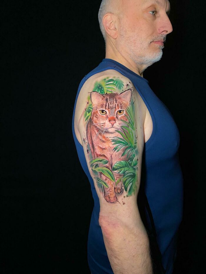 Man showing a colorful cat tattoo on his upper arm, a beautiful tribute turning memories of pets into tattoos.
