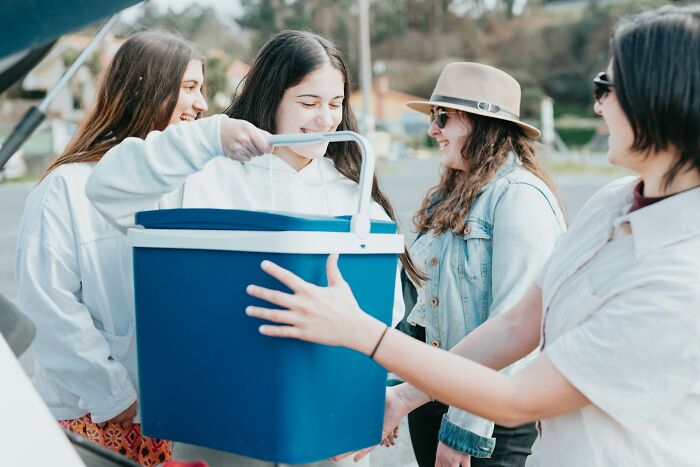 Group of friends smiling while holding a large cooler, surrounded by lost things owners never came back for.