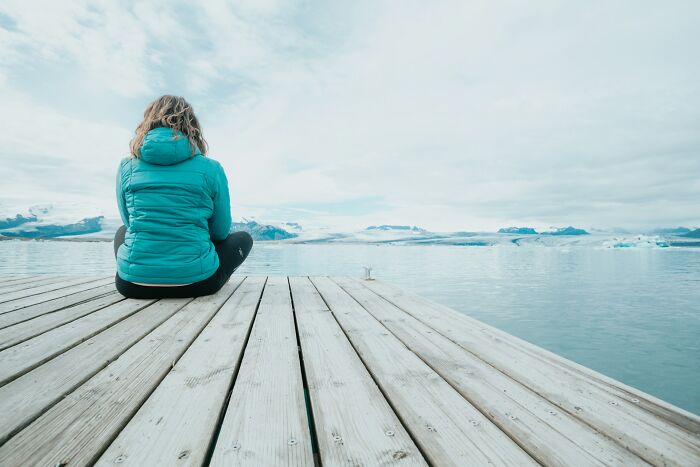 Person in turquoise jacket sitting on wooden dock facing icy water and mountains, reflecting on surprising life facts.