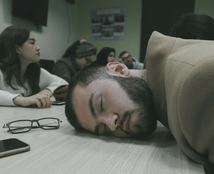 Man with beard resting head on table while others in background look away, capturing reactions after dark secrets revealed.