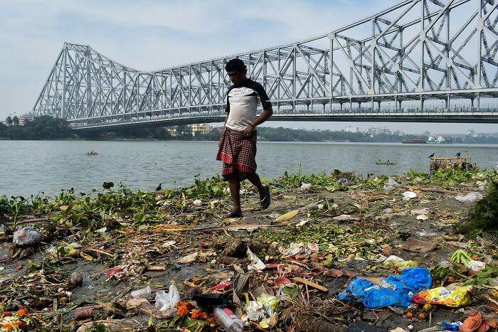 Man walks on polluted riverbank near large steel bridge, illustrating disturbing facts people learned against their will
