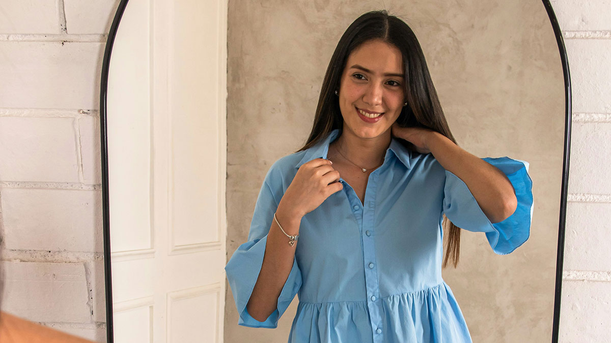 Young woman in a blue blouse smiling and adjusting her hair while looking in a mirror, family drama atmosphere.