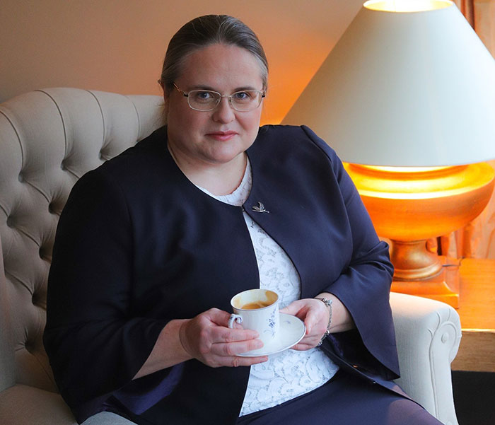 Woman in glasses holding a cup, seated indoors near a lamp, related to Lithuania lawmaker’s cat consent news. Woman in glasses holding a cup, seated indoors near a lamp, related to Lithuania lawmaker’s cat consent news.