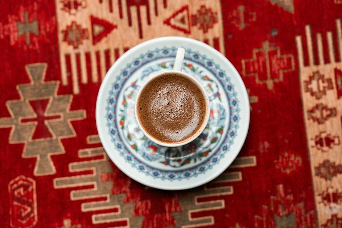Cup of traditional Greek coffee on a decorative saucer placed on a vibrant red patterned Greek village rug Cup of traditional Greek coffee on a decorative saucer placed on a vibrant red patterned Greek village rug