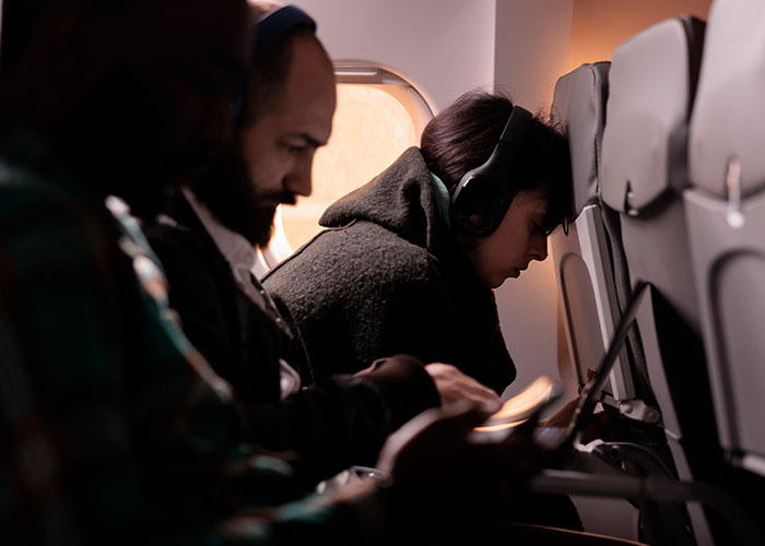 Passenger parents and kids wearing headphones on an airplane to reduce noise during the flight.