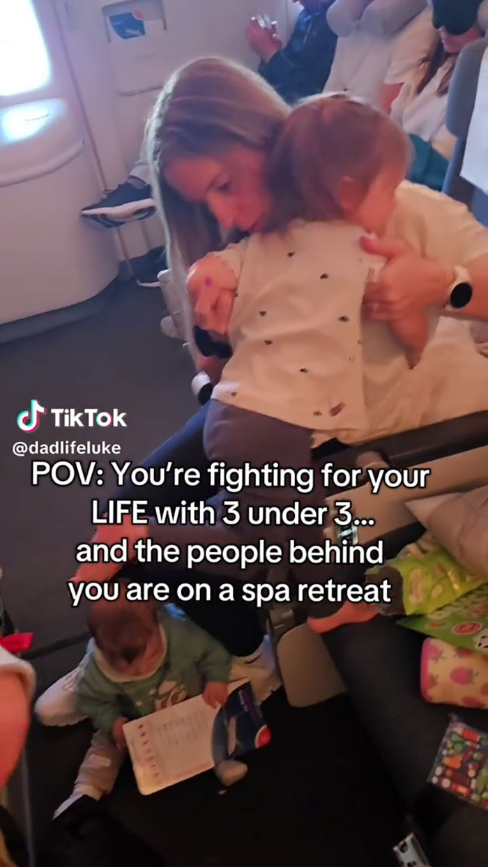 Parent comforting toddler on airplane while another child plays on the floor, highlighting airplane parents kids noise challenges.