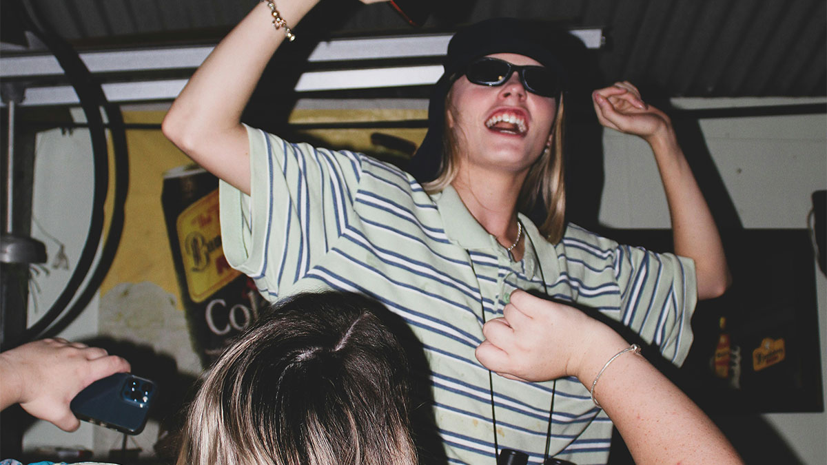 Young woman wearing sunglasses dancing energetically with friends, highlighting chaotic best friend dynamics and social distancing.