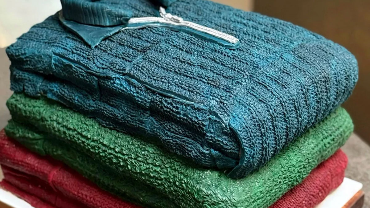 Stack of masterfully crafted cakes designed to look like folded textured sweaters, showcasing creative cake art.