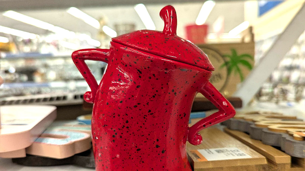 Red ceramic coffee pot with arms on hips, found among other items in a secondhand store display.