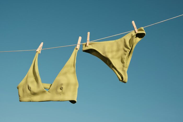 Green bikini top and bottom hanging on a clothesline against a clear blue sky, illustrating everyday things done wrong.