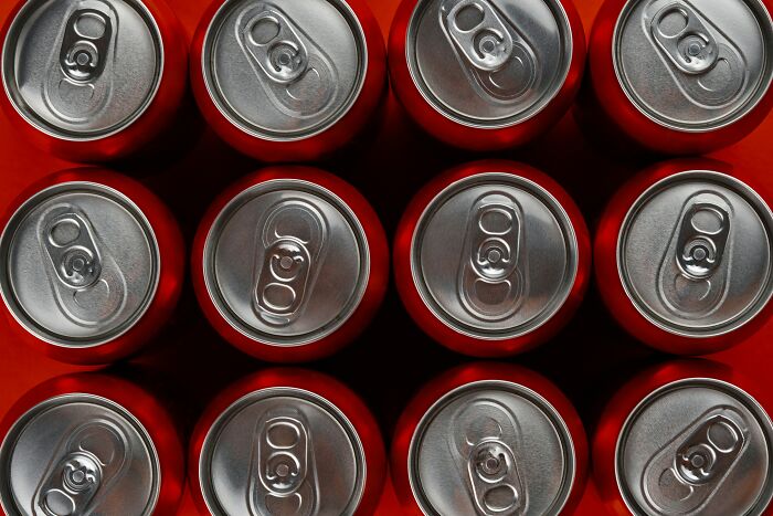Overhead view of unopened soda cans arranged on red surface, symbolizing people who became rich out of nowhere.