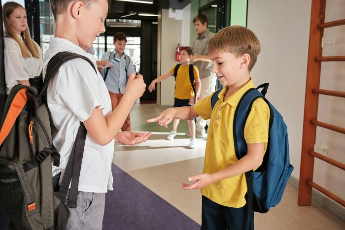 Two schoolboys with backpacks playing rock-paper-scissors indoors, capturing a moment before possible revenge stories unfold.