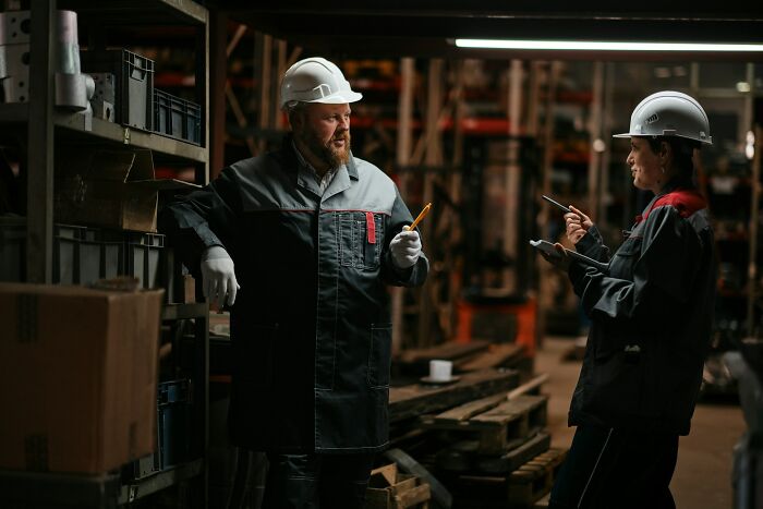 Two factory workers wearing helmets discussing plans, showcasing incredible minds proving you don’t need a degree to be genius.