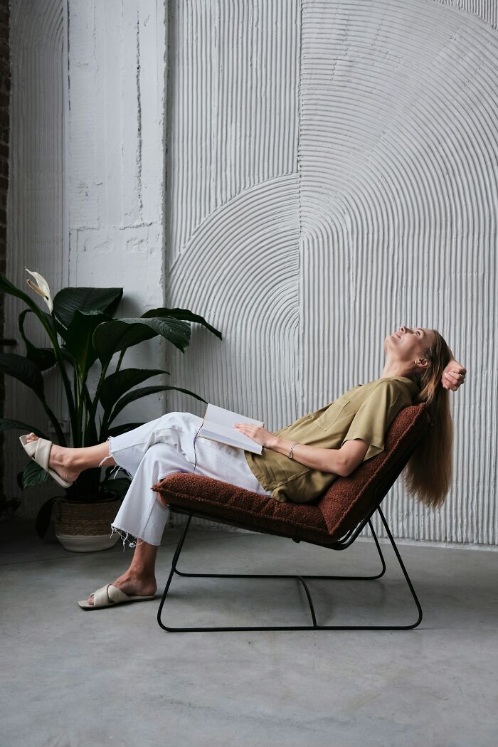 Woman reading a book while reclining on a chair in a modern room symbolizing incredible minds without a degree genius.