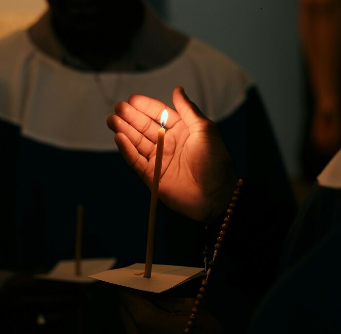 Hand shielding a candle flame during a dark ceremony, illustrating true stories that sound completely made up but happened.