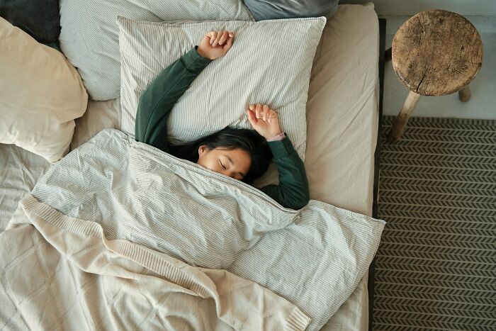 Person sleeping in bed with arms raised, highlighting everyday things that can be more dangerous for your health than you realize.
