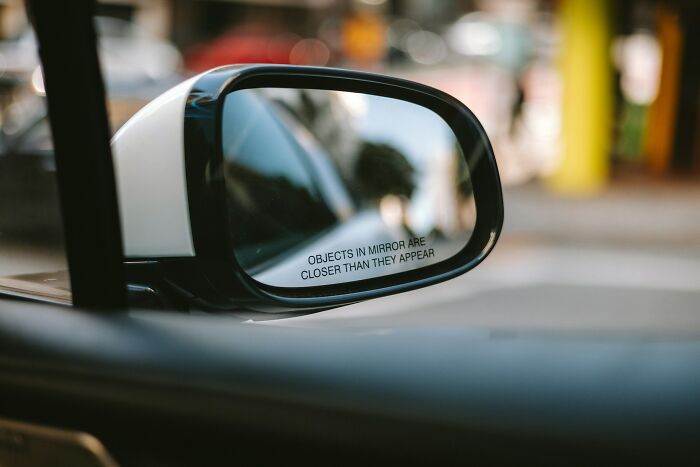 Car side mirror reflecting a blurred street scene, illustrating secrets people trust strangers online with.