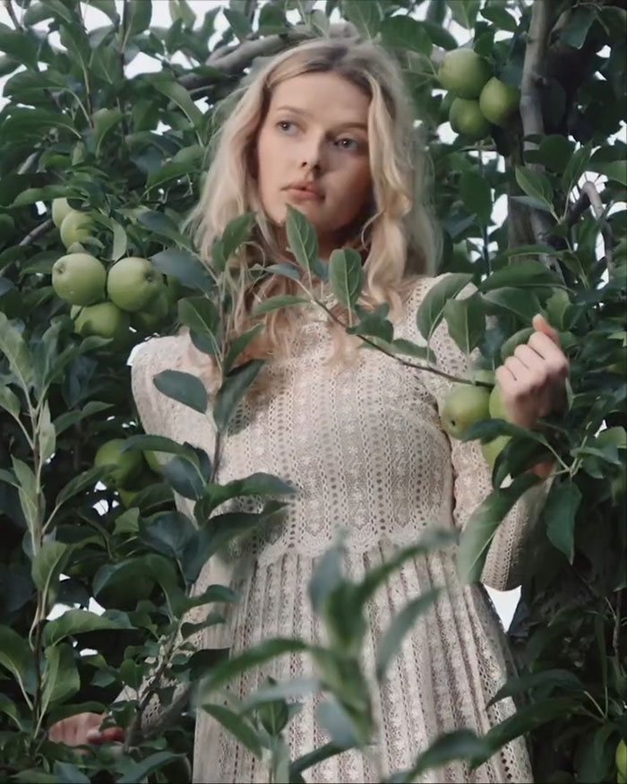 Apple Martin posing among green apples in a lace dress for a self-portrait modeling campaign announcement video.