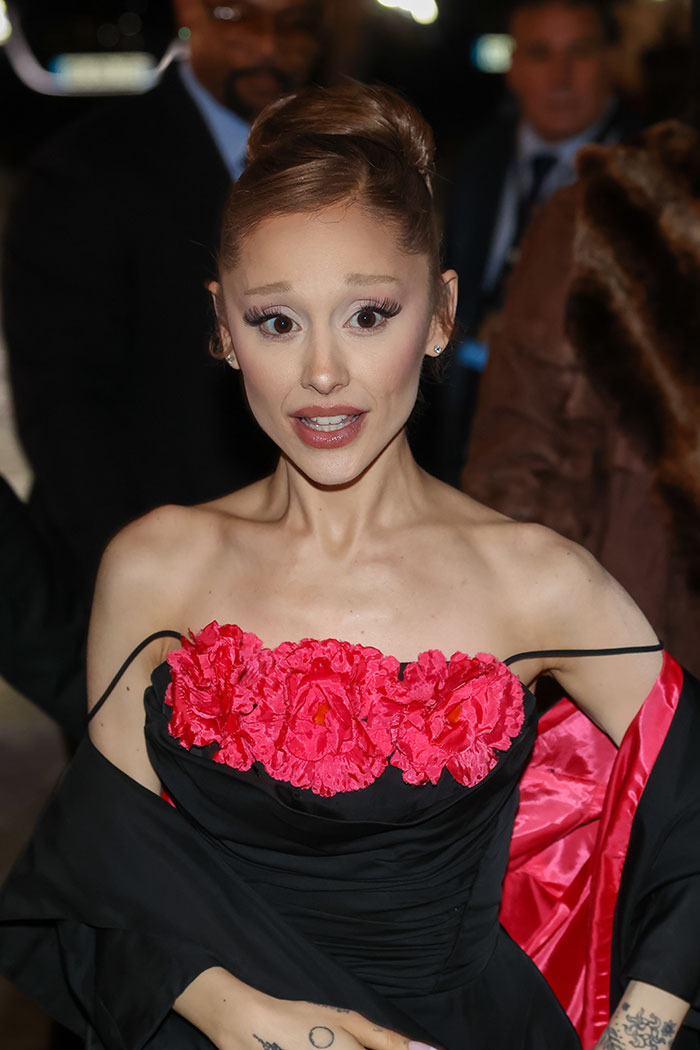 Ariana Grande attending an event wearing a black dress with red floral detailing, addressing body-shaming concerns.
