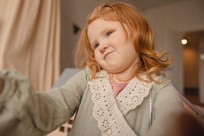 Young girl with red hair making a playful face indoors, capturing aunt pay niece tummy tuck drama mood.