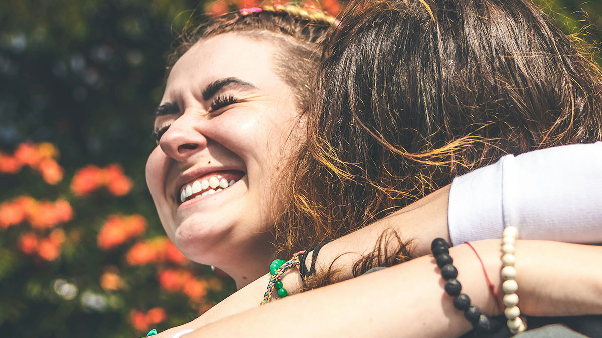 Two women hugging outdoors, one smiling brightly, capturing a joyful moment amid aunt pay niece tummy tuck drama.