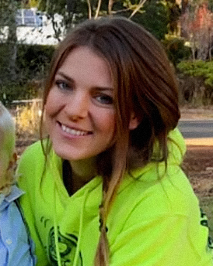 Young mom, 31, smiling outdoors, wearing a bright yellow hoodie, highlighting plastic surgery travel to Vietnam risks.