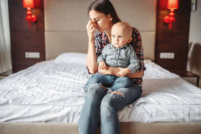 Woman heartbroken sitting on bed holding baby, upset about husband ditching her and baby on Christmas day. Woman heartbroken sitting on bed holding baby, upset about husband ditching her and baby on Christmas day.