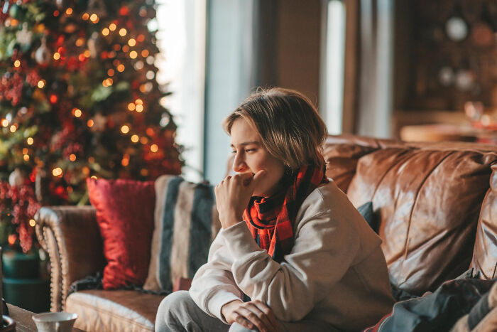 Wife heartbroken sitting alone on couch near Christmas tree with sad expression during holiday season at home Wife heartbroken sitting alone on couch near Christmas tree with sad expression during holiday season at home