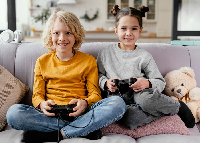 Two kids playing video games on couch, illustrating family babysitting expectations and demands for payment. Two kids playing video games on couch, illustrating family babysitting expectations and demands for payment.