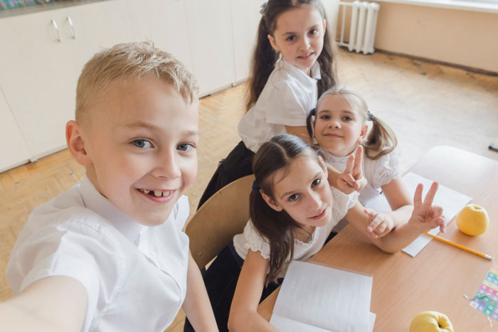 Four kids sitting at a table as one takes a selfie, illustrating family babysitting expectations and sibling dynamics. Four kids sitting at a table as one takes a selfie, illustrating family babysitting expectations and sibling dynamics.