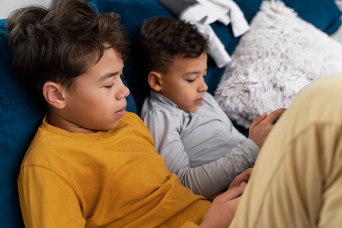 Two kids relaxing on a couch, focused on their devices while babysit sister watches during hockey day. Two kids relaxing on a couch, focused on their devices while babysit sister watches during hockey day.