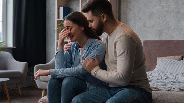 Young woman sitting upset while man comforts her indoors, illustrating babysit sister kids hockey challenges. Young woman sitting upset while man comforts her indoors, illustrating babysit sister kids hockey challenges.