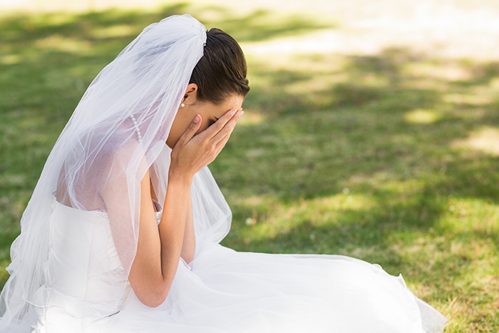Bride in wedding dress sitting outdoors covering her face, upset after discovering groom cheated with her mom. Bride in wedding dress sitting outdoors covering her face, upset after discovering groom cheated with her mom.