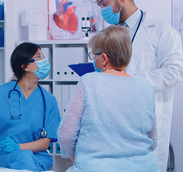 Medical team wearing masks consulting with an elderly patient, representing chaotic good healthcare moments.