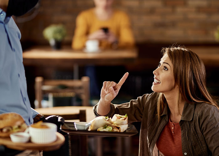 Customer discussing industry secrets with server at restaurant while pointing finger during meal service.