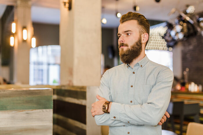 Bearded man with arms crossed standing thoughtfully indoors, representing the biggest bullet dodged in life moments.