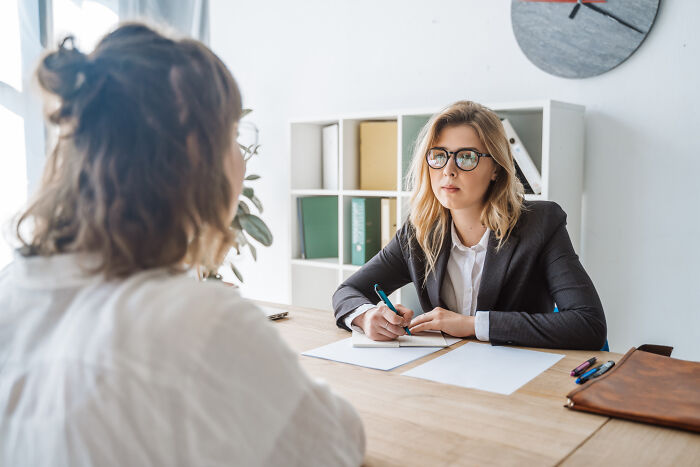 Two women in a professional office setting, one taking notes during a serious conversation about biggest bullet dodged.