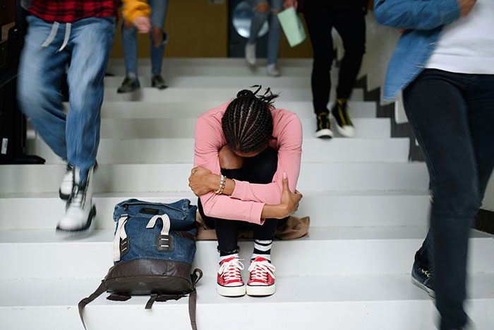 Teen sitting alone on stairs with head down surrounded by people, illustrating deepest secrets people refuse to reveal to parents