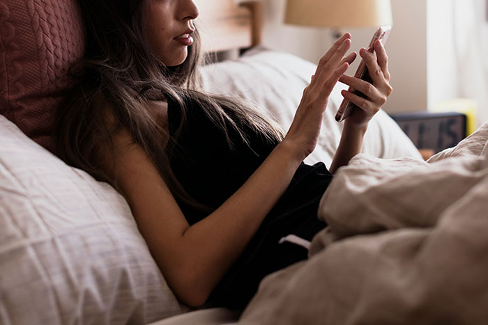 Young woman lying in bed, looking intently at her phone, reflecting on the deepest secrets people refuse to reveal to parents.