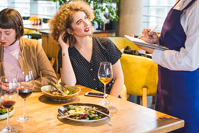 Woman dining out looking entitled while waitress serves a perfect dish of revenge in a restaurant setting.